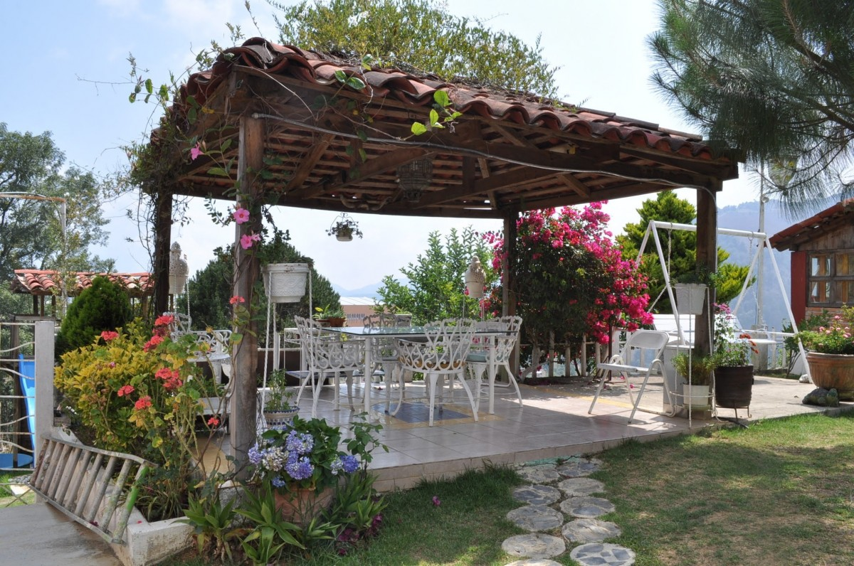 Zděná pergola s taškovou střechou porostlá popínavými rostlinami, pod ní zahradní sezení
